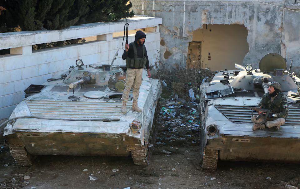 Rebel fighters talk together as one of them stands on a military vehicle holding a weapon in the town of Tel Rifaat, Syria December 2, 2024.