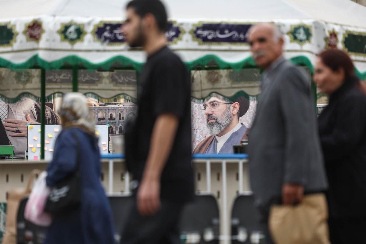 People walk past a banner depicting Iran's supreme leader Mojtaba Khamenei and his slain father, Ali, near Tehran's grand bazaar, May 16, 2026