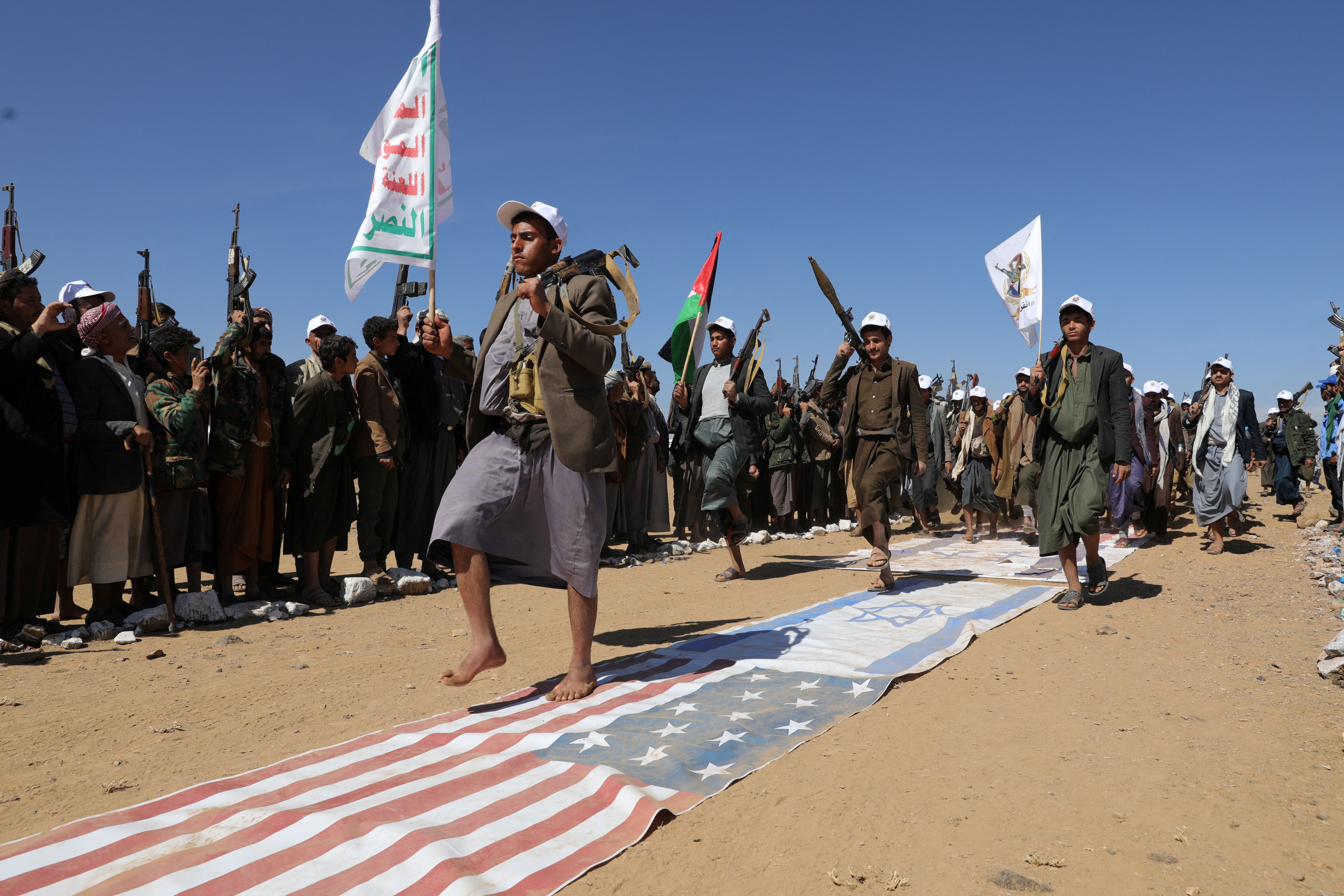 Tribesmen loyal to the Houthis march on US and Israeli flags during a military parade for new tribal recruits amid escalating tensions with the US-led coalition in the Red Sea, in Bani Hushaish, Yemen January 22, 2024.