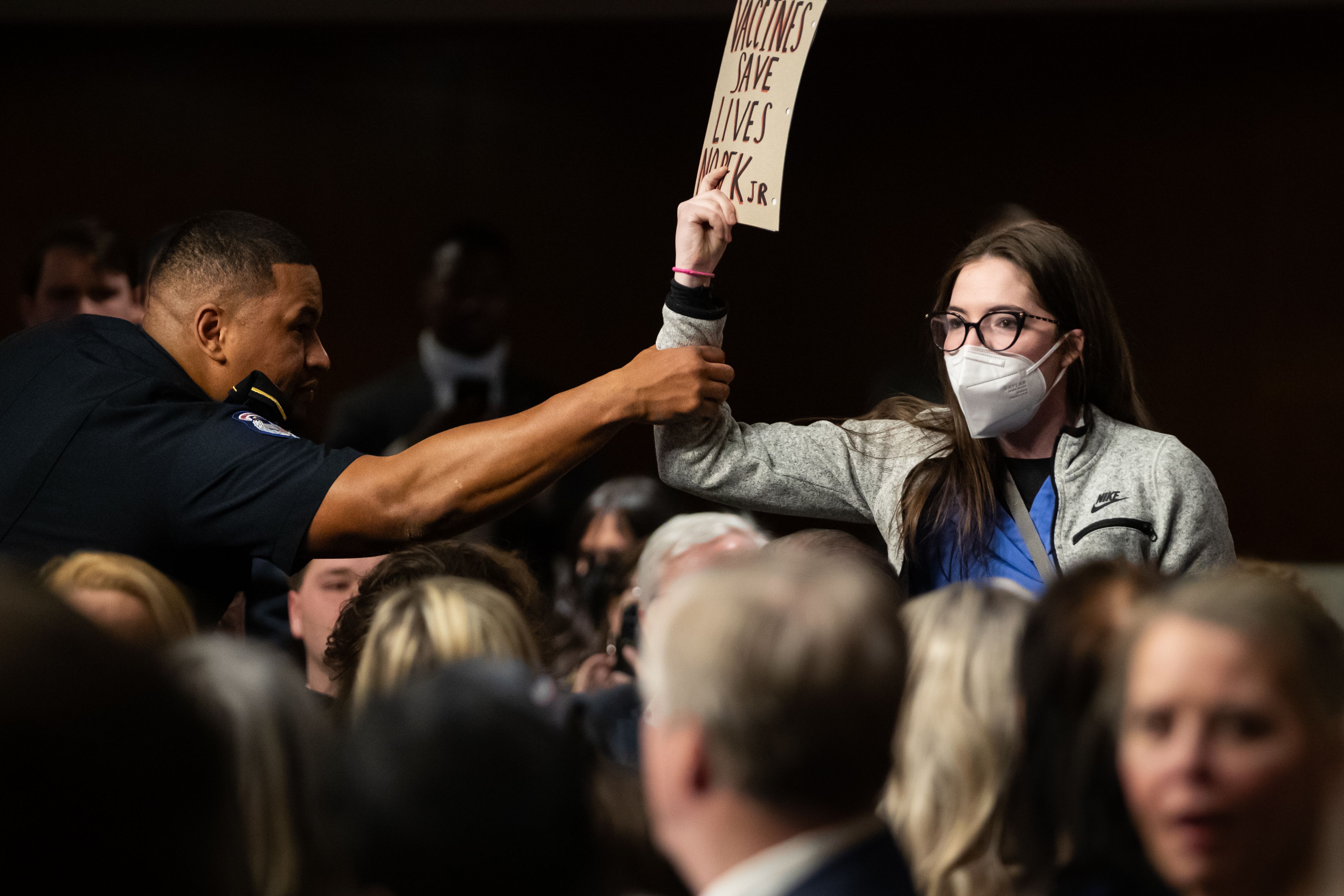 یک نیروی پلیس چهارشنبه دهم بهمن در جلسه کمیته مالی سنای آمریکا برای بررسی صلاحیت رابرت اف کندی، گزینه ترامپ به عنوان وزیر بهداشت، در حال بیرون کردن فرد معترضی است که این جلسه را مختل کرده است. این فرد در اعتراض به مواضع کندی در مخالفت با واکسیناسیون، نوشته‌ای نمایش می‌دهد که می‌گوید: «واکسن زندگی انسان‌ها را نجات می‌دهد»