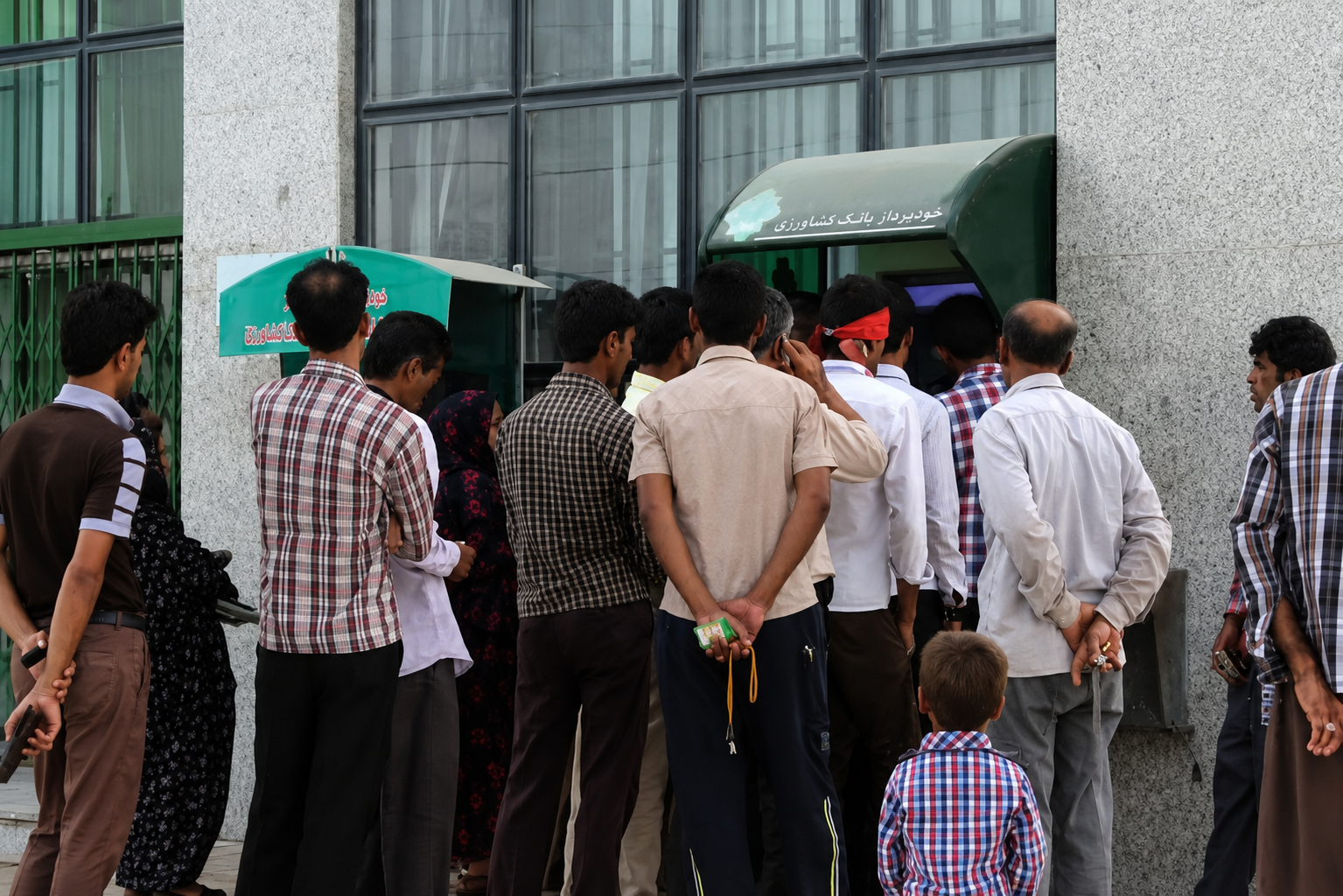 File photo of people queue at an ATM in an Iranian city as customers seek access to banking services.