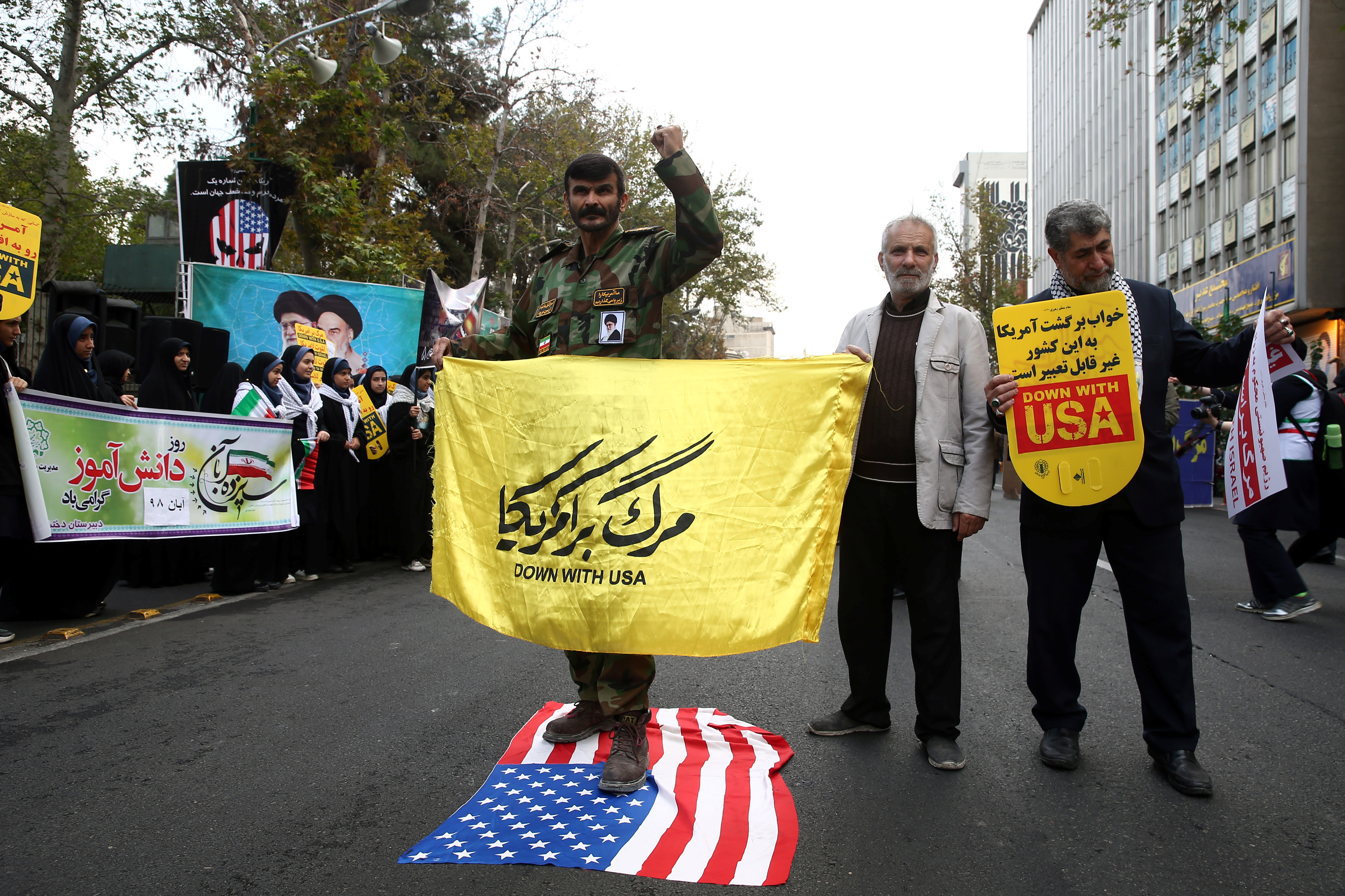 An Iranian man stands on a US flag, as they attend an anti US demonstration, marking the 40th anniversary of the U.S. embassy takeover, near the old US embassy in Tehran, Iran November 4, 2019.