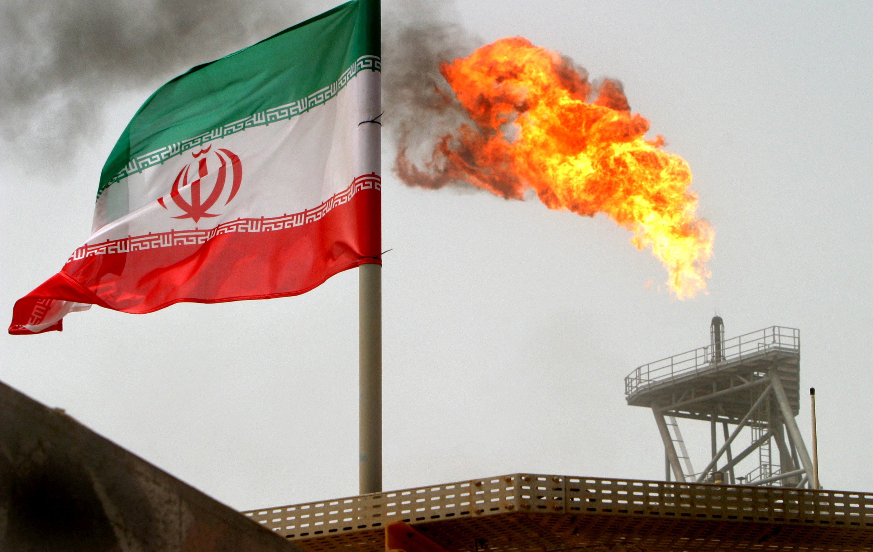A gas flare on an oil production platform is seen alongside an Iranian flag in the Persian Gulf, July 25, 2005. 