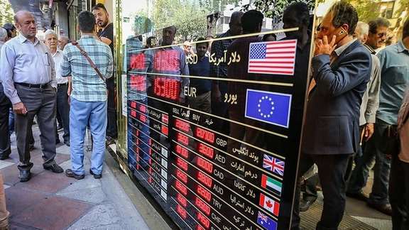 People looking at a board that shows exchange rates against rial