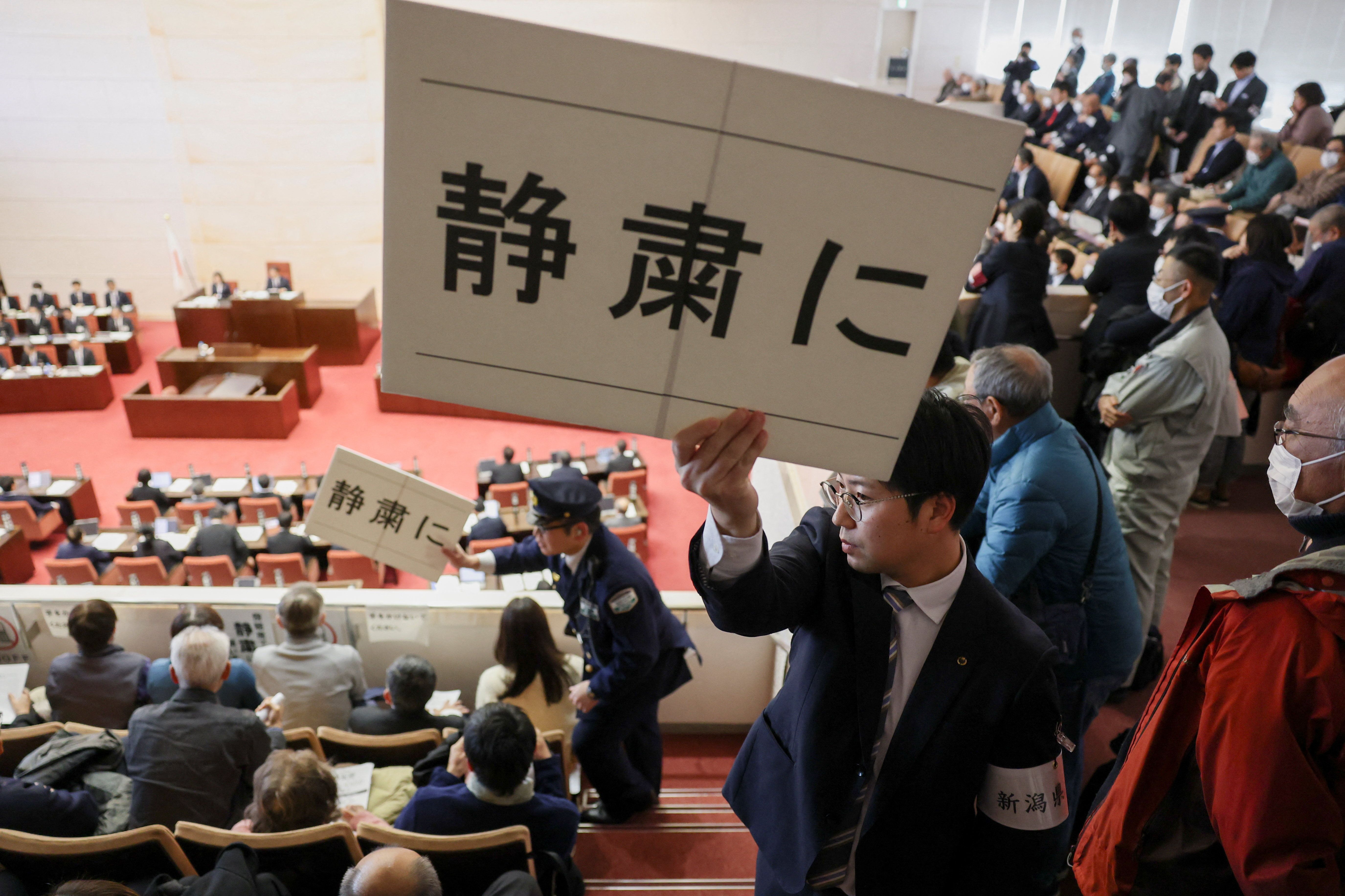 افسران امنیتی در نشست پارلمان محلی پلاکاردهایی در دست داشتند که روی آن‌ها نوشته شده بود: «لطفا سکوت را رعایت کنید»