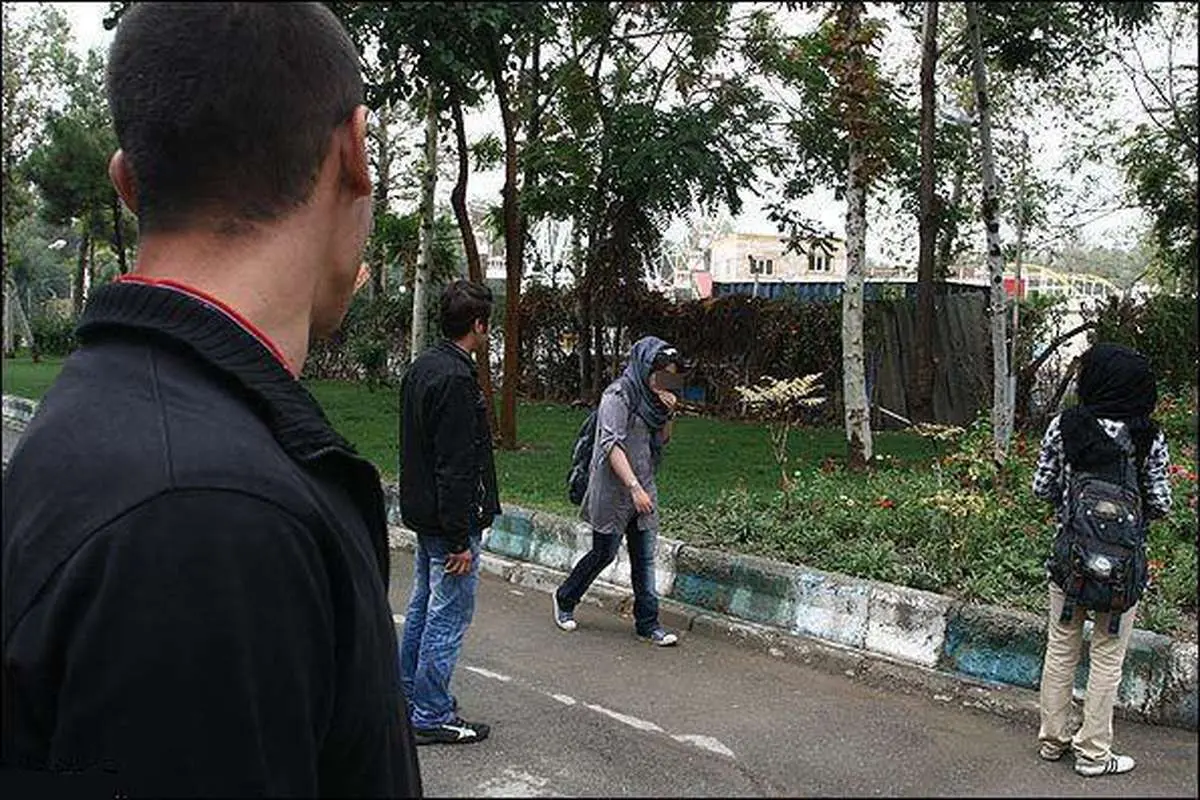 Two young women walk along a sidewalk while being closely watched and harassed by some men. (Undated)