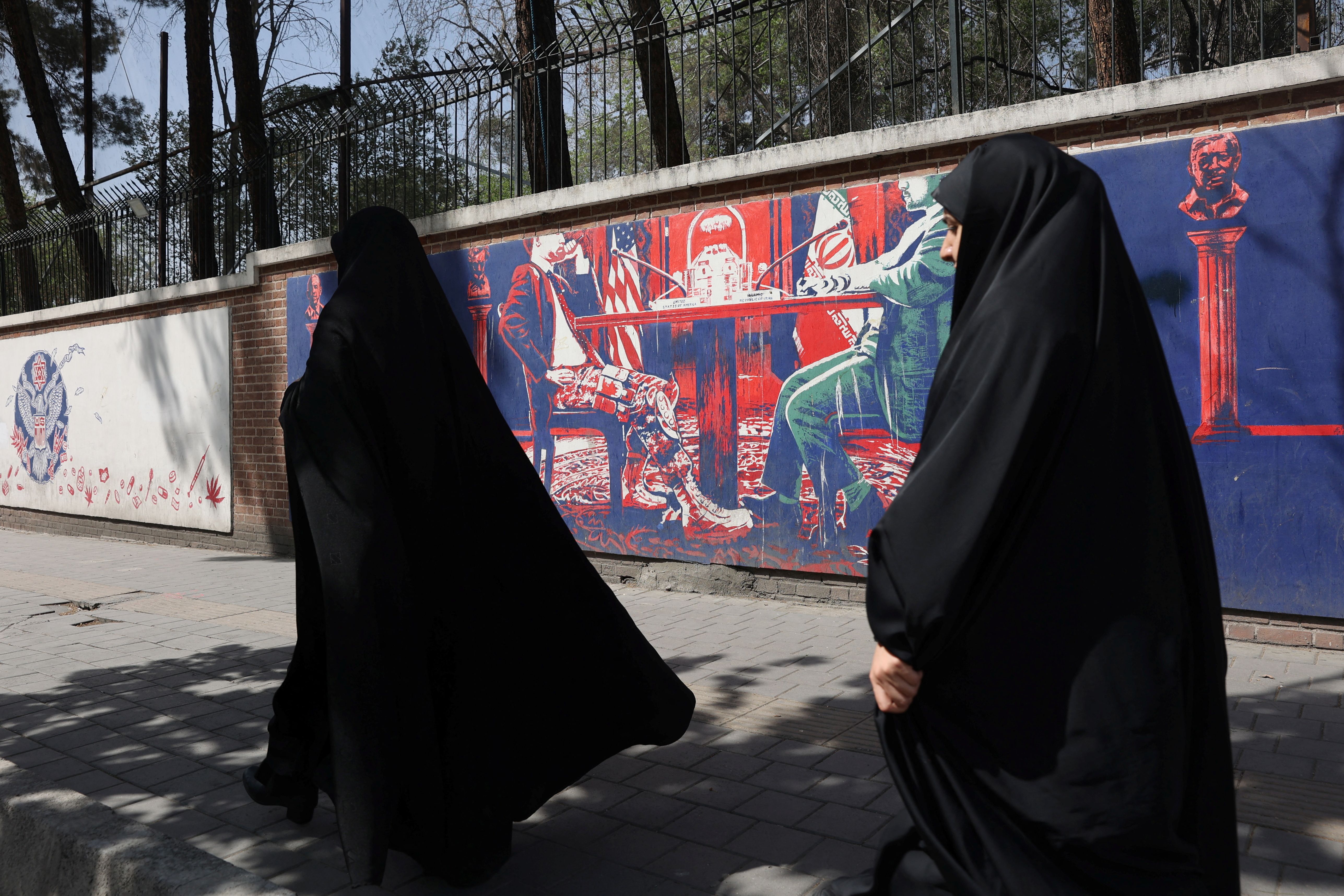 Two Iranian women walking past a mural against the negotiations with Washington, Tehran (April 2025) 