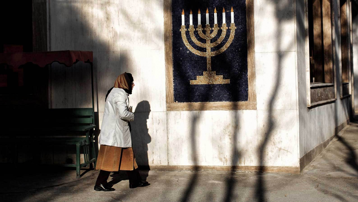 A woman walks past a mosaic of a menorah outside a Jewish synagogue in Iran