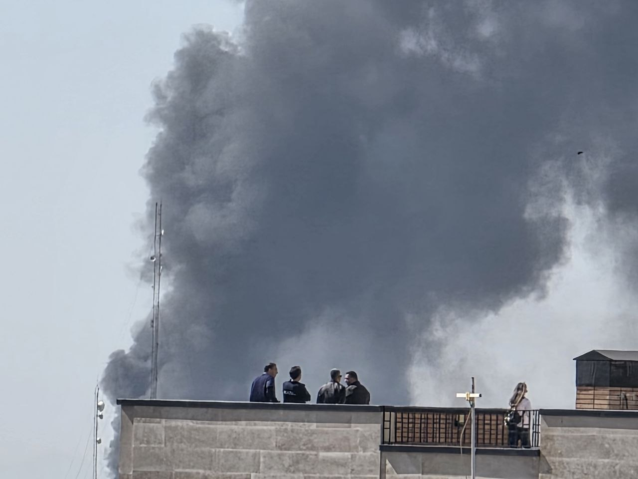 Residents watch as a large plume of smoke rises over Tehran following Israeli-US strikes.