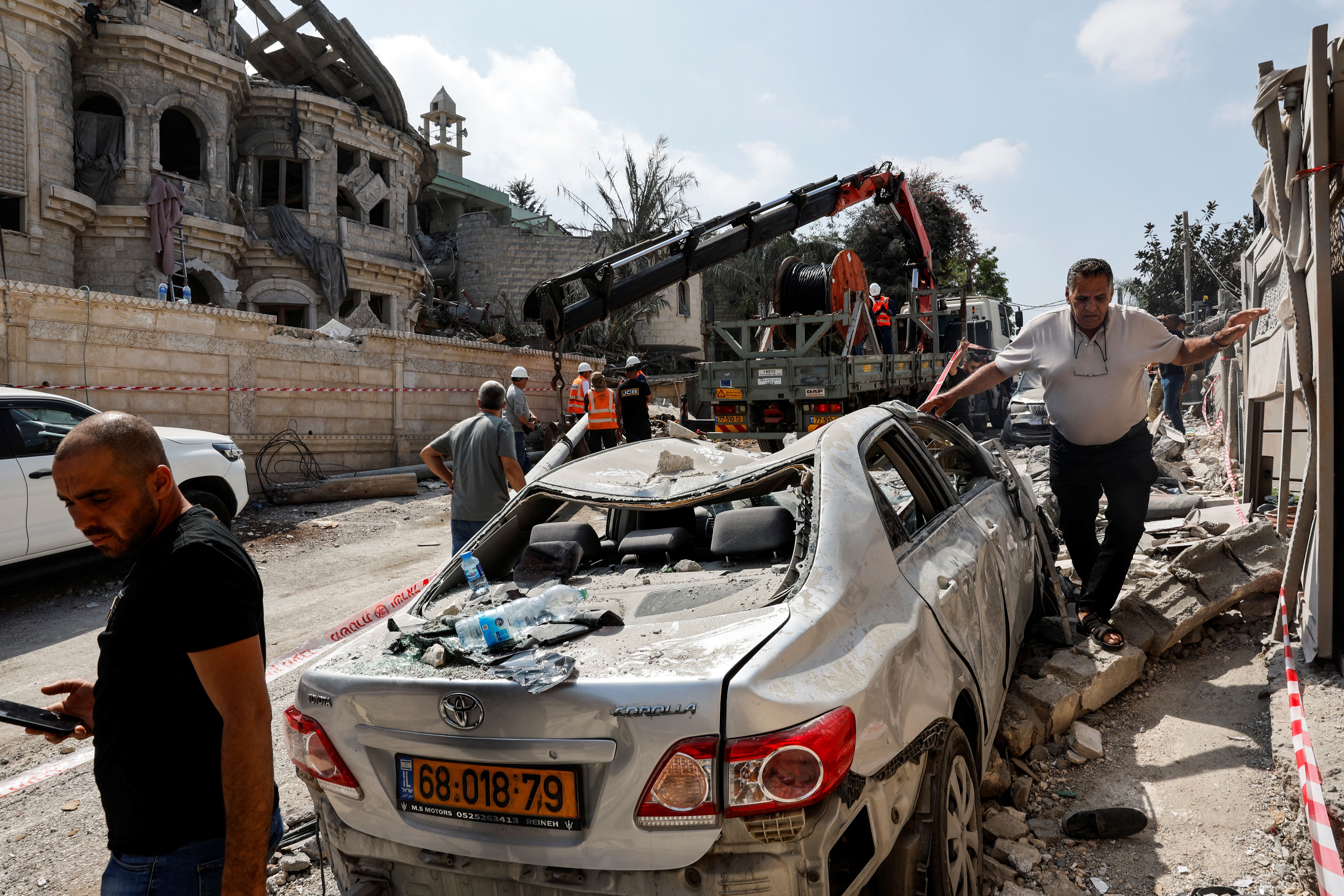 Men walk near a damaged vehicle at an impact site following missile attack from Iran, in northern Israel, in Tamra, Israel, June 15, 2025.