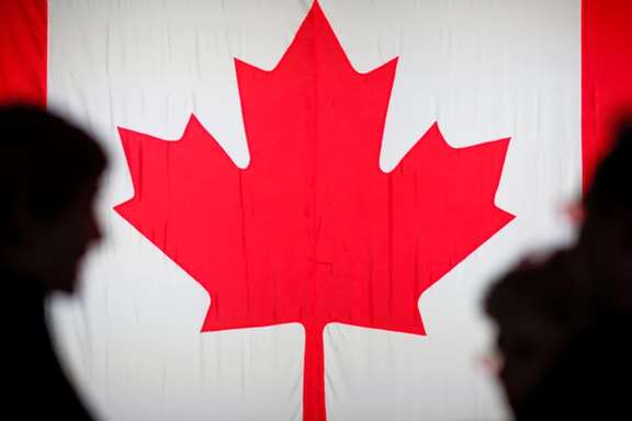 People are silhouetted in front of the Canadian national flag in Montreal, Quebec, Canada.