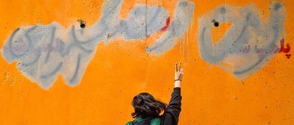 An Iranian woman standing in front of a wall with the main slogan of the ongoing protests – Women, Life, Liberty – seen despite the government’s attempts to cover it