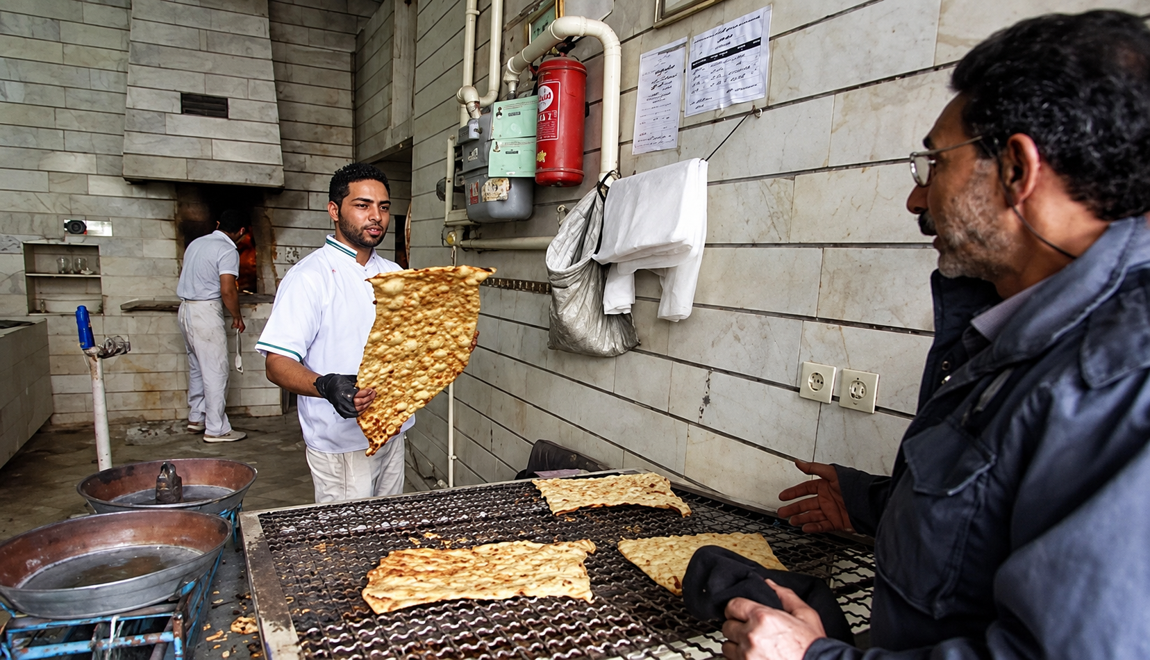 A baker serves a customer at a bakery in Iran. Rising prices have led some customers to buy bread on credit.