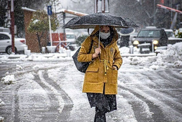 A masked pedestrian walks under heavy snowfall, shielding themselves with an umbrella as winter intensifies, causing widespread closures and disruptions across Iran. (Undated)