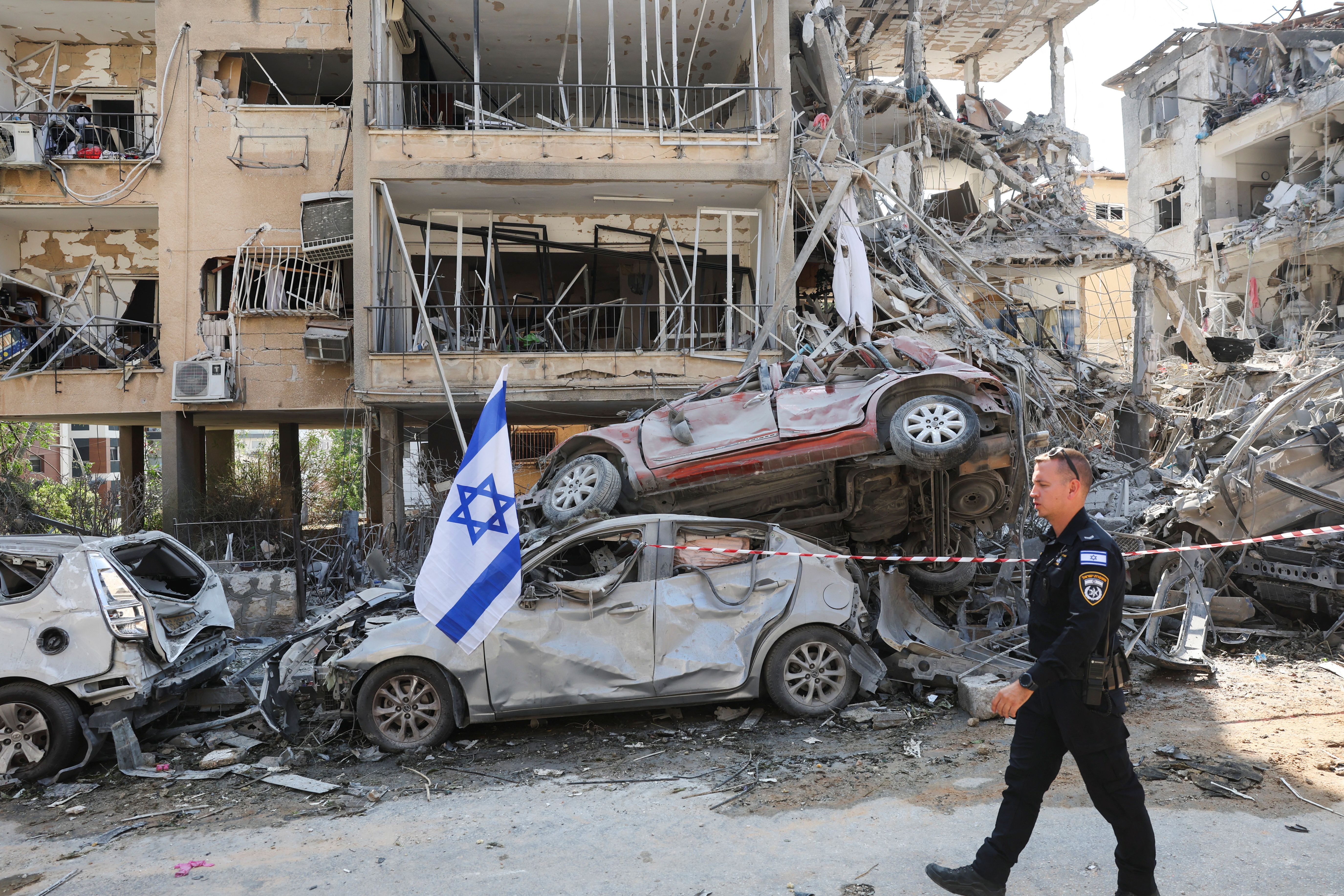 An Israeli police officer walks past damaged vehicles at an impact site following missile attack from Iran on Israel, in Ramat Gan, Israel, June 14, 2025.