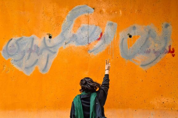 An Iranian woman standing in front of a wall on which the main slogan of the ongoing protests – Women, Life, Liberty – is seen despite the government’s attempts to cover it