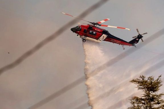 A helicopter drops water on the Palisades Fire, one of several simultaneous blazes that have ripped across Los Angeles County, along Mandeville Canyon, in the Encino neighborhood of Los Angeles, California, US, January 11, 2025.