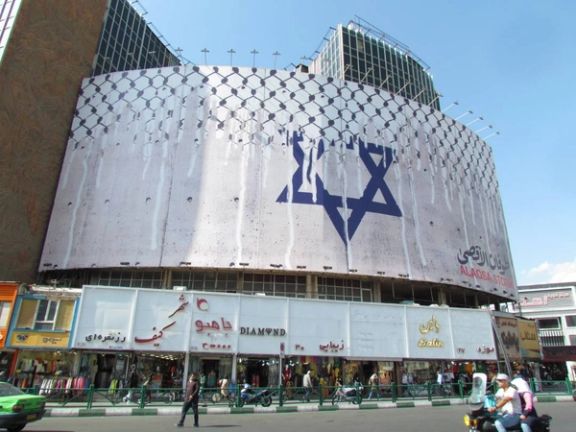 People walk past an anti-Israel billboard with the chequered Keffiyeh covering the Star of David in Tehran's central Vali-Asr square. (October 2023)