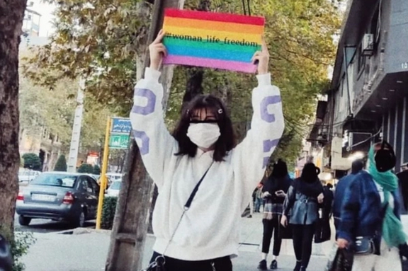 یک معترض در ایران بدون حجاب اجباری، پرچم رنگین کمان را در خیابان حمل کرد