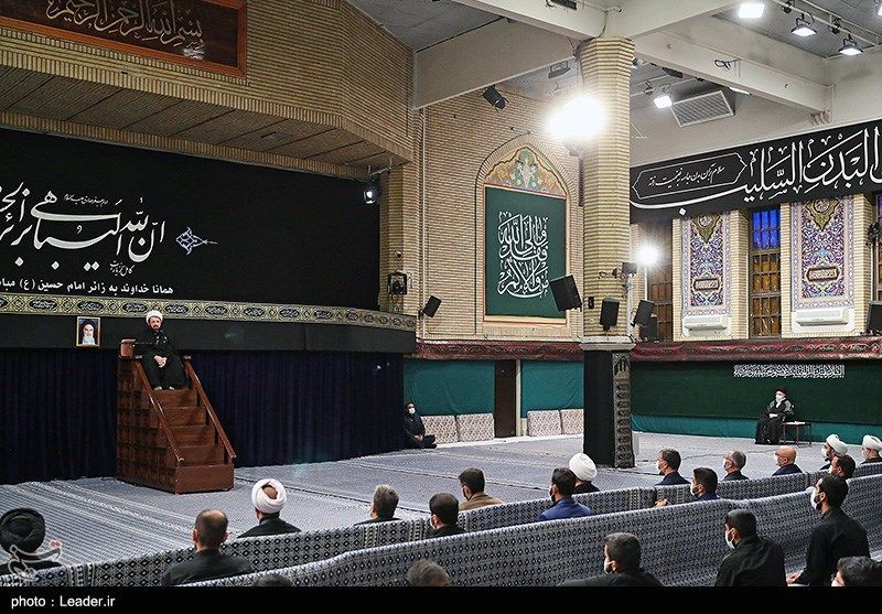 Khamenei sitting to the far right of the hall as a preacher speaks at the traditional manbar