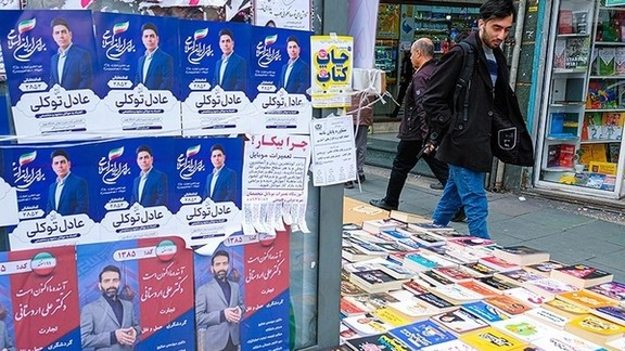 An Iranian man walks past campaign posters for the parliamentary election in Tehran, February 2024