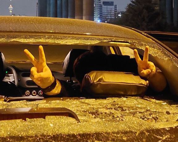 نماد پیروزی شهروند معترض از شیشههای شکسته یک خودرو