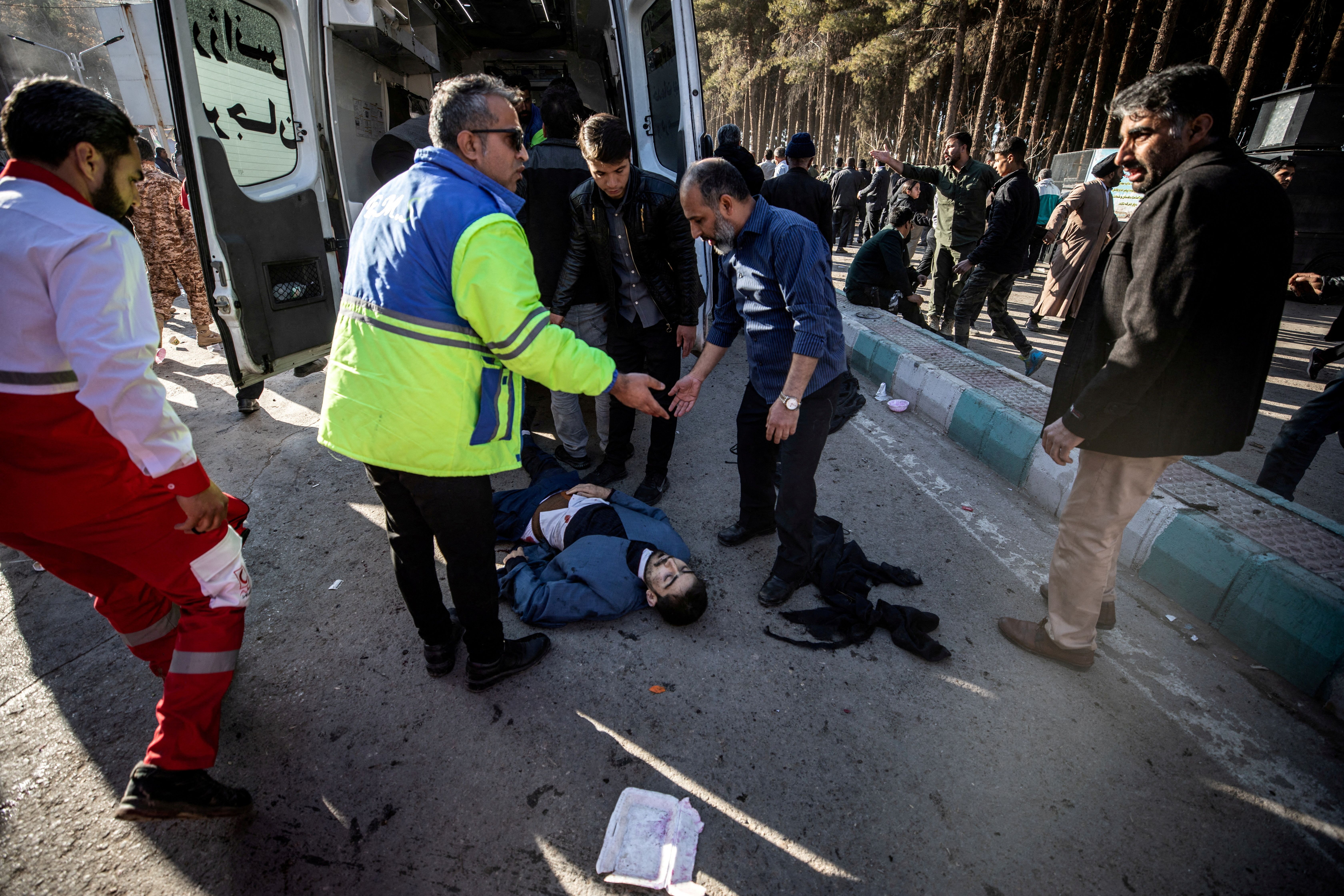 People stand near a man lying on the ground at the scene of explosions during a ceremony held to mark the death of late Iranian General Qassem Soleimani, in Kerman, Iran, January 3, 2024.