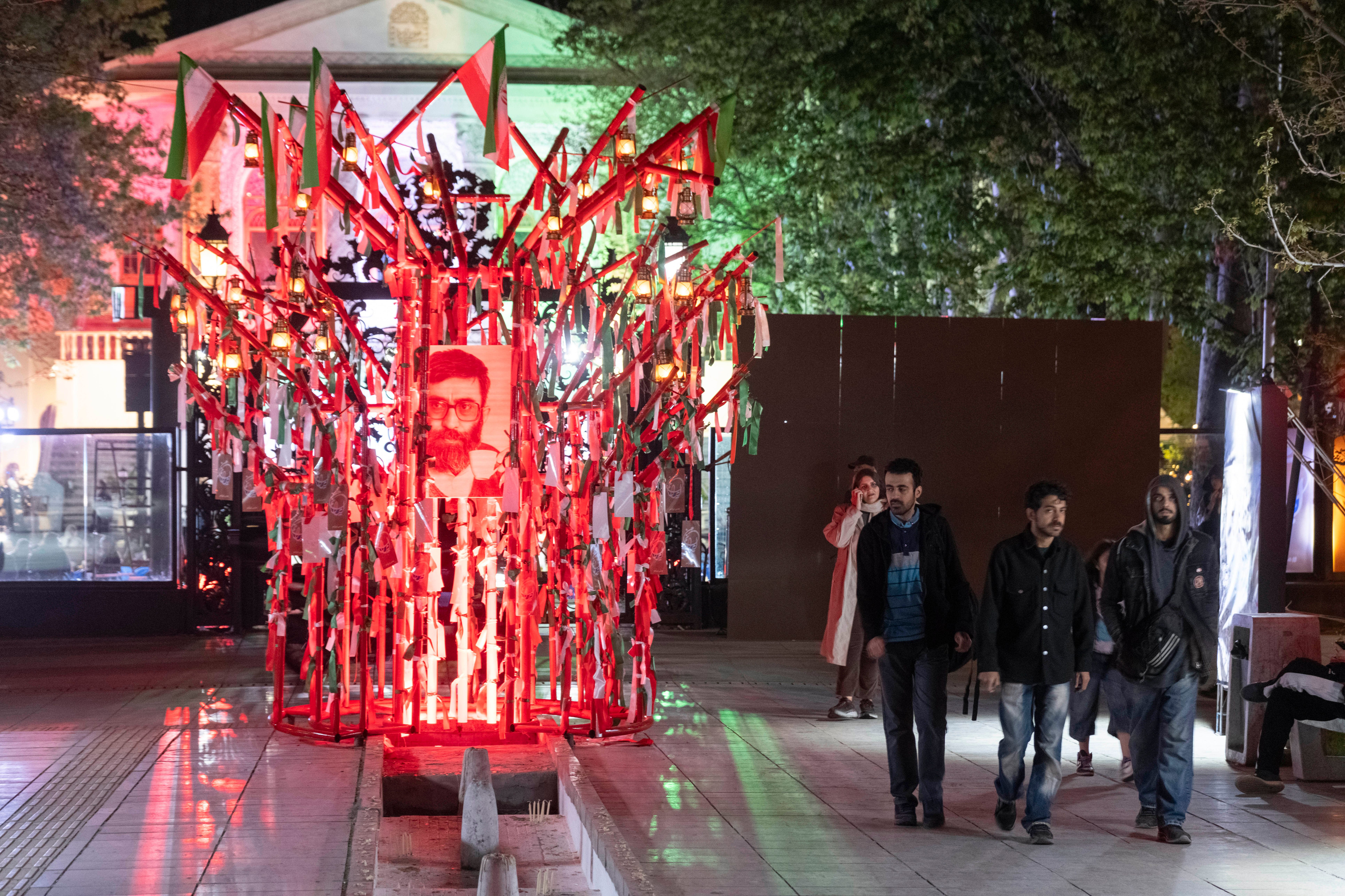 People walk past a religious symbol with a portrait of Iran's slain Supreme Leader Ali Khamenei in northern Tehran on April 12, 2026.