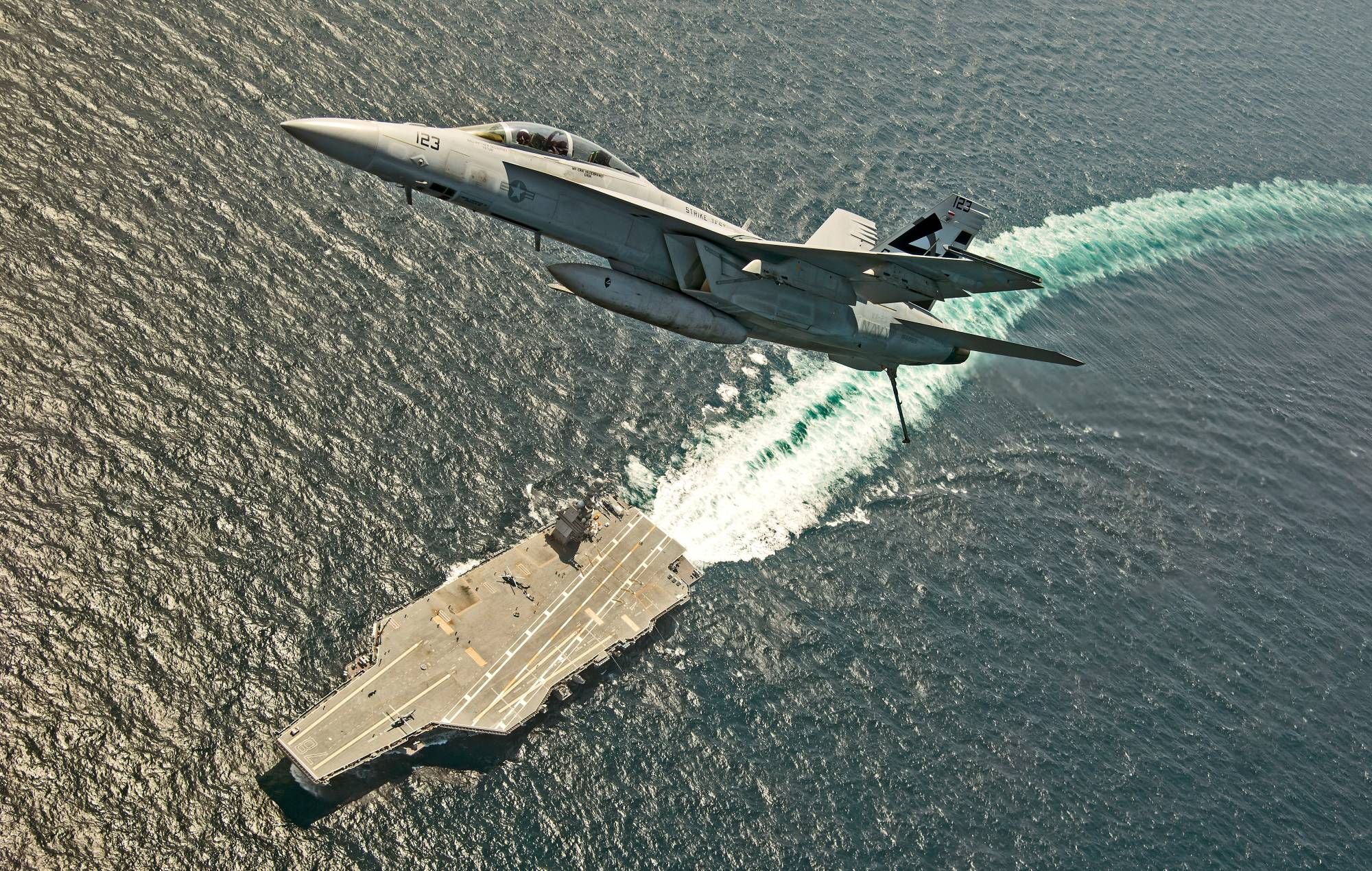 An F/A-18F Super Hornet jet flies over the USS Gerald R. Ford in the Atlantic Ocean in July 2017.