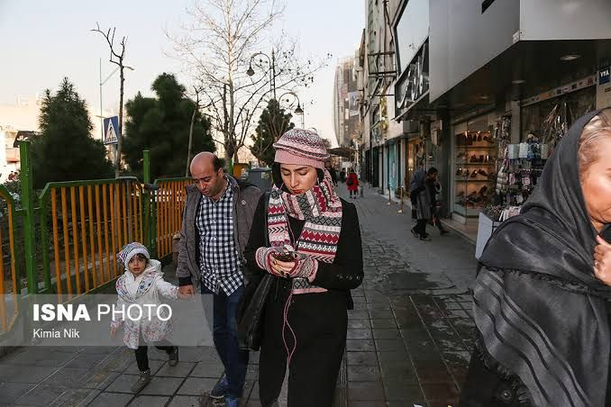 People looking at their cellphones on a street in Tehran (undated)