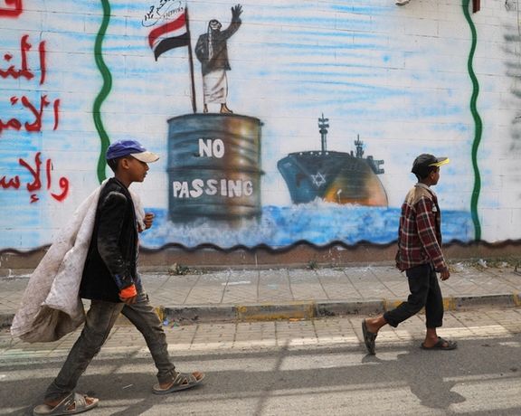 People walk past a graffiti, depicting a Houthi fighter stopping an Israeli ship off the coast of Yemen, painted on a wall of the Saudi embassy in Sanaa, Yemen February 15, 2024.