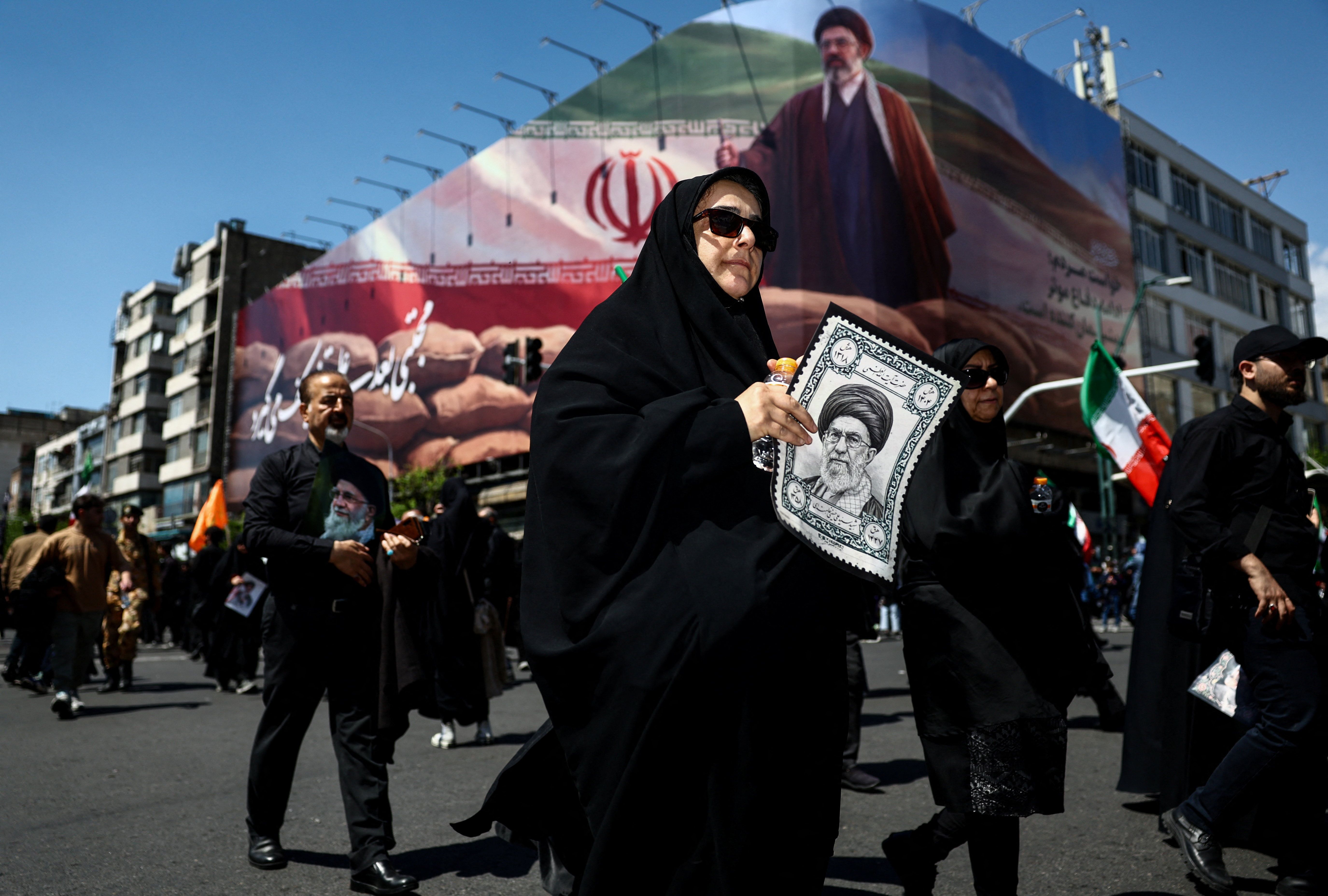 A person holds an image of late Supreme Leader Ali Khamenei, with an image of Iran's new Supreme Leader Mojtaba Khamenei on a billboard in the background, on the day of a ceremony marking 40 days since Khamenei was killed in Israeli and US strikes, in Tehran, Iran, April 9, 2026. 