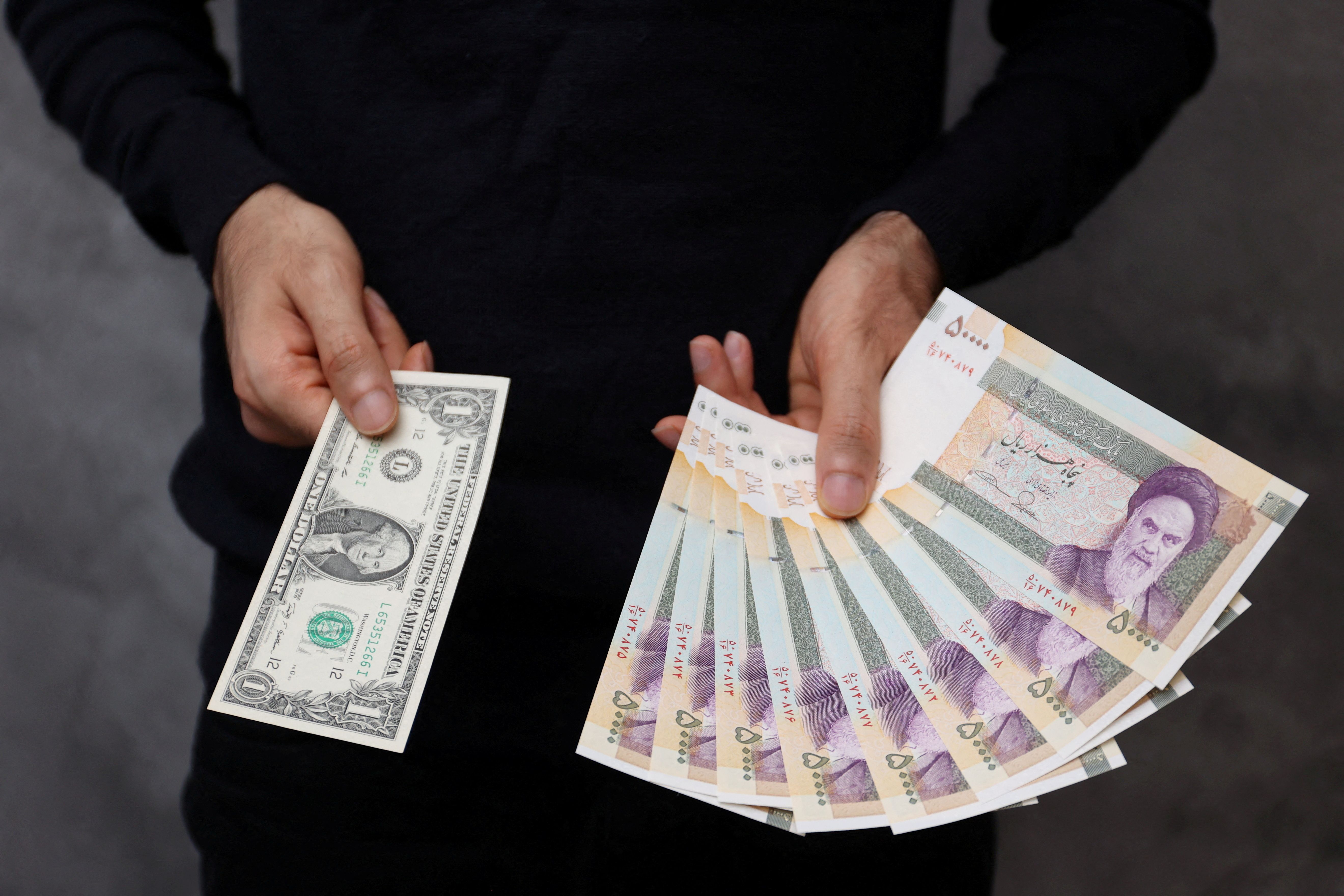 A currency dealer poses for a photo with a U.S one dollar bill and the amount being given when converting it into Iranian rials in an exchange shop in Tehran, Iran December 25, 2022