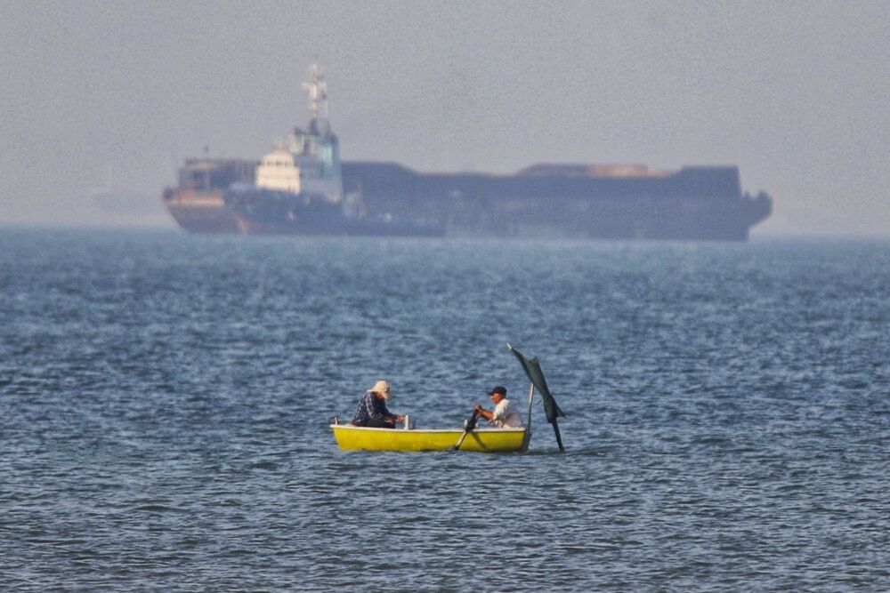 photo shows a small fishing boat in the Strait of Hormuz with an oil tanker in the background near Iran’s southern coast.
