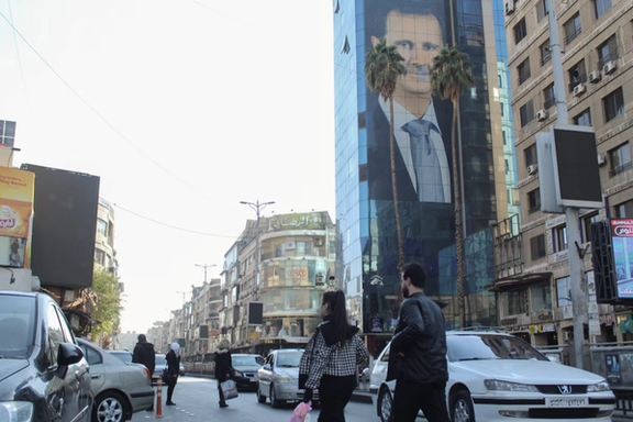 People walk near a poster depicting Syria's President Bashar al-Assad in Damascus, after last week's rebel seizure of Aleppo marked the biggest offensive for years, Syria December 5, 2024. REUTERS