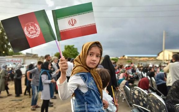 An Afghan girl holding the flags of the Islamic Republic of Iran and Afghanistan