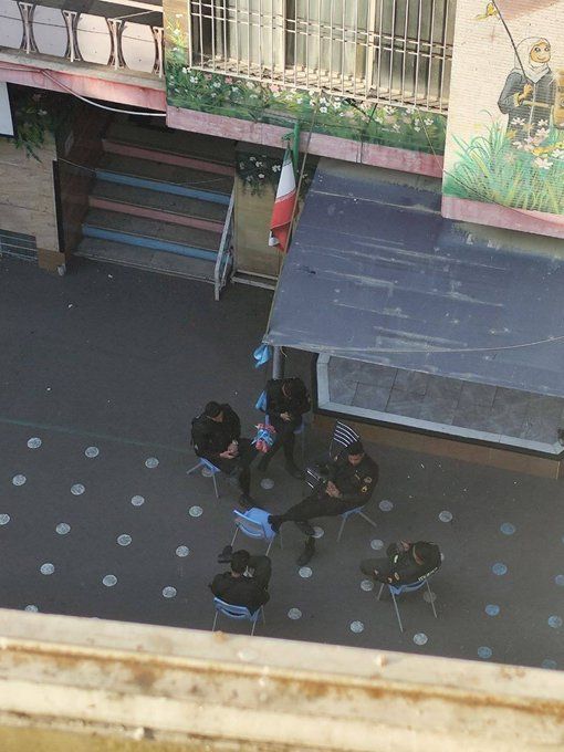 Uniformed officers sit in a school courtyard beneath an Iranian flag in an image  shared on social media on March 3, 2026.
