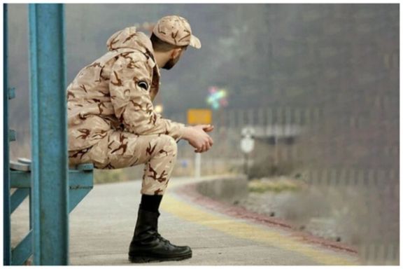A conscript sitting on a metal bench at a train station in Iran
